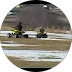 Two military tanks positioned on a snowy, muddy field with a few trees in the background.
