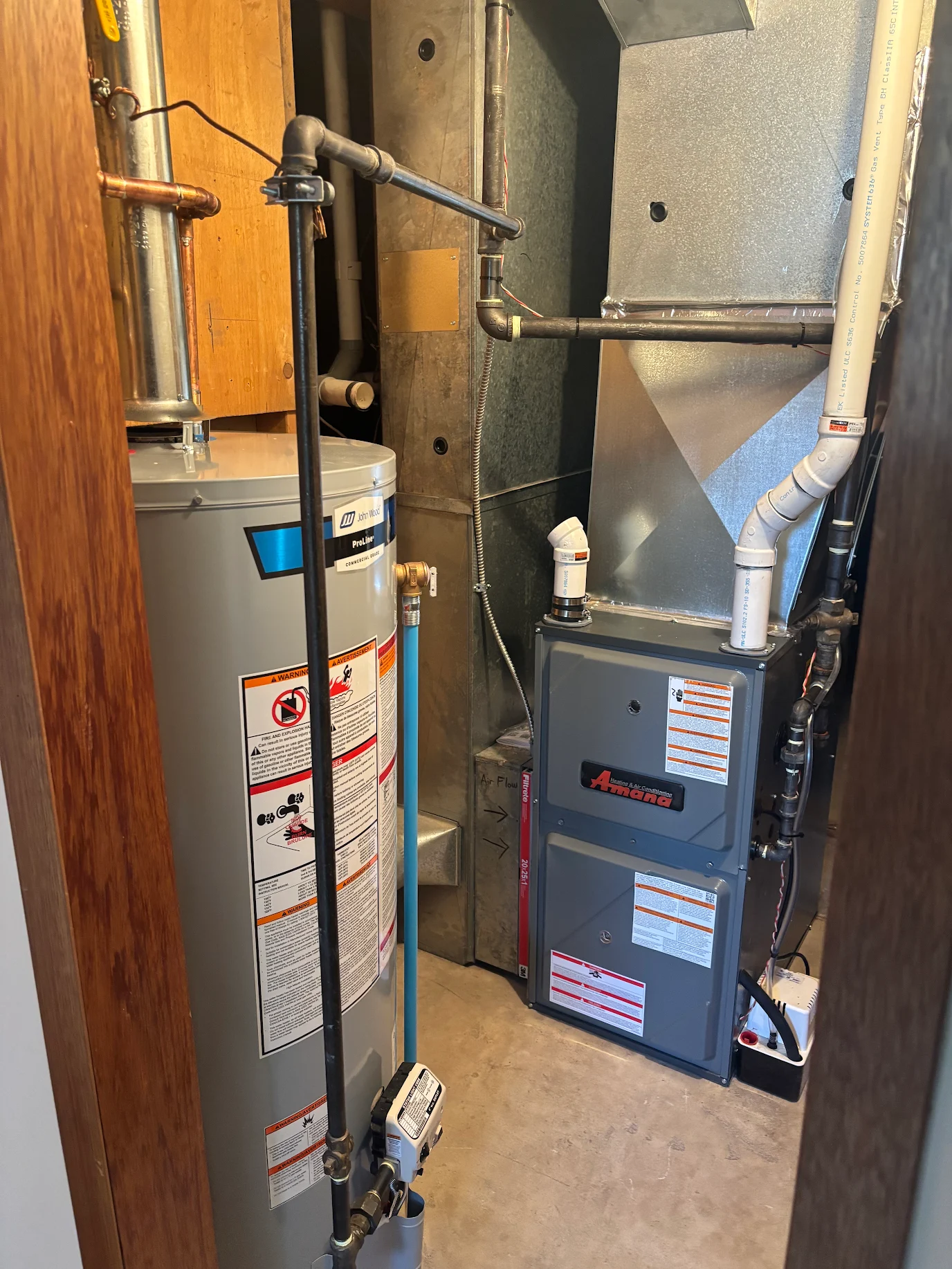 Water heater and Amana furnace installed in a narrow utility closet with pipes and vents.