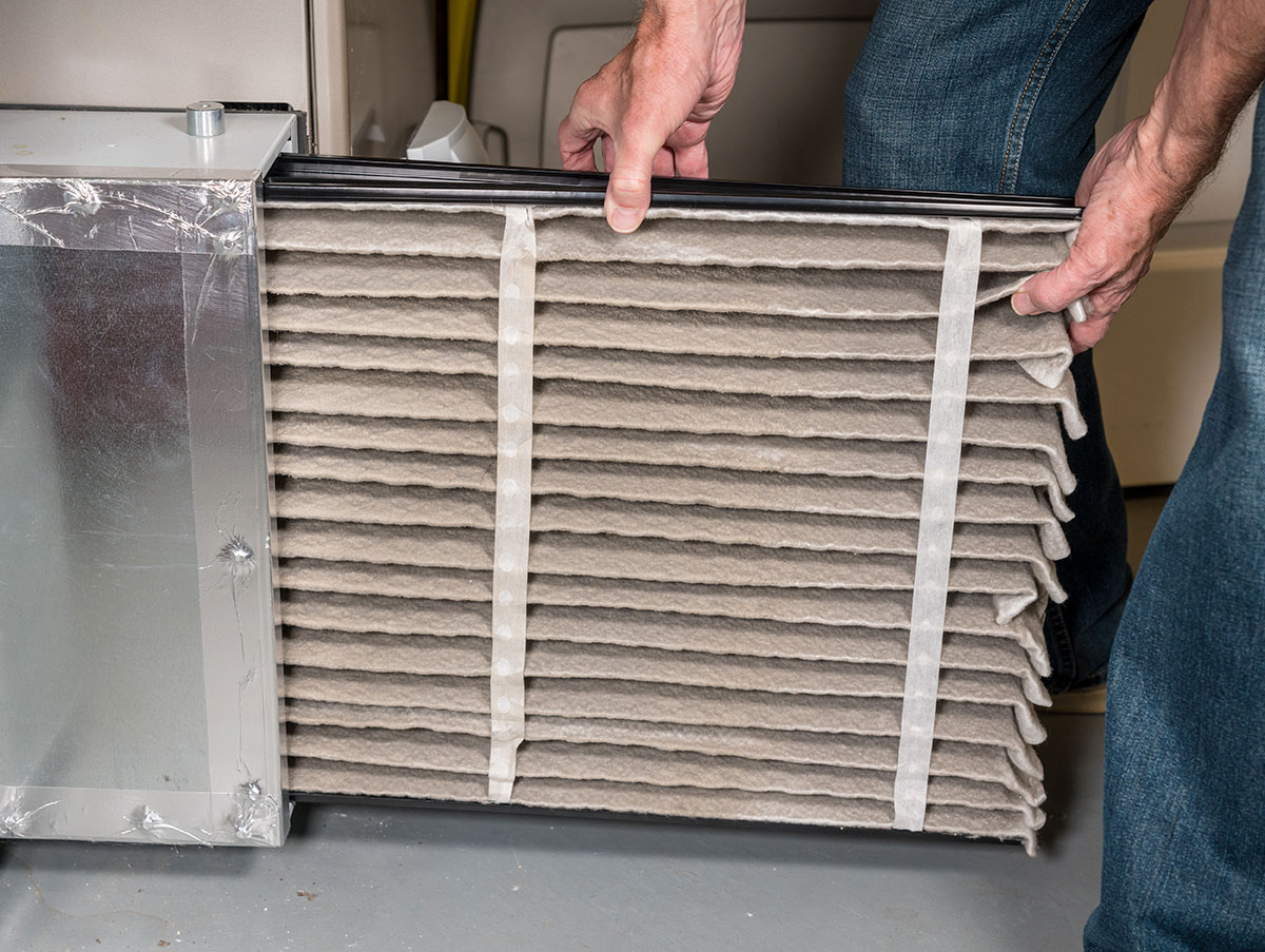 Person wearing jeans changing a large rectangular air filter in a metal HVAC unit.