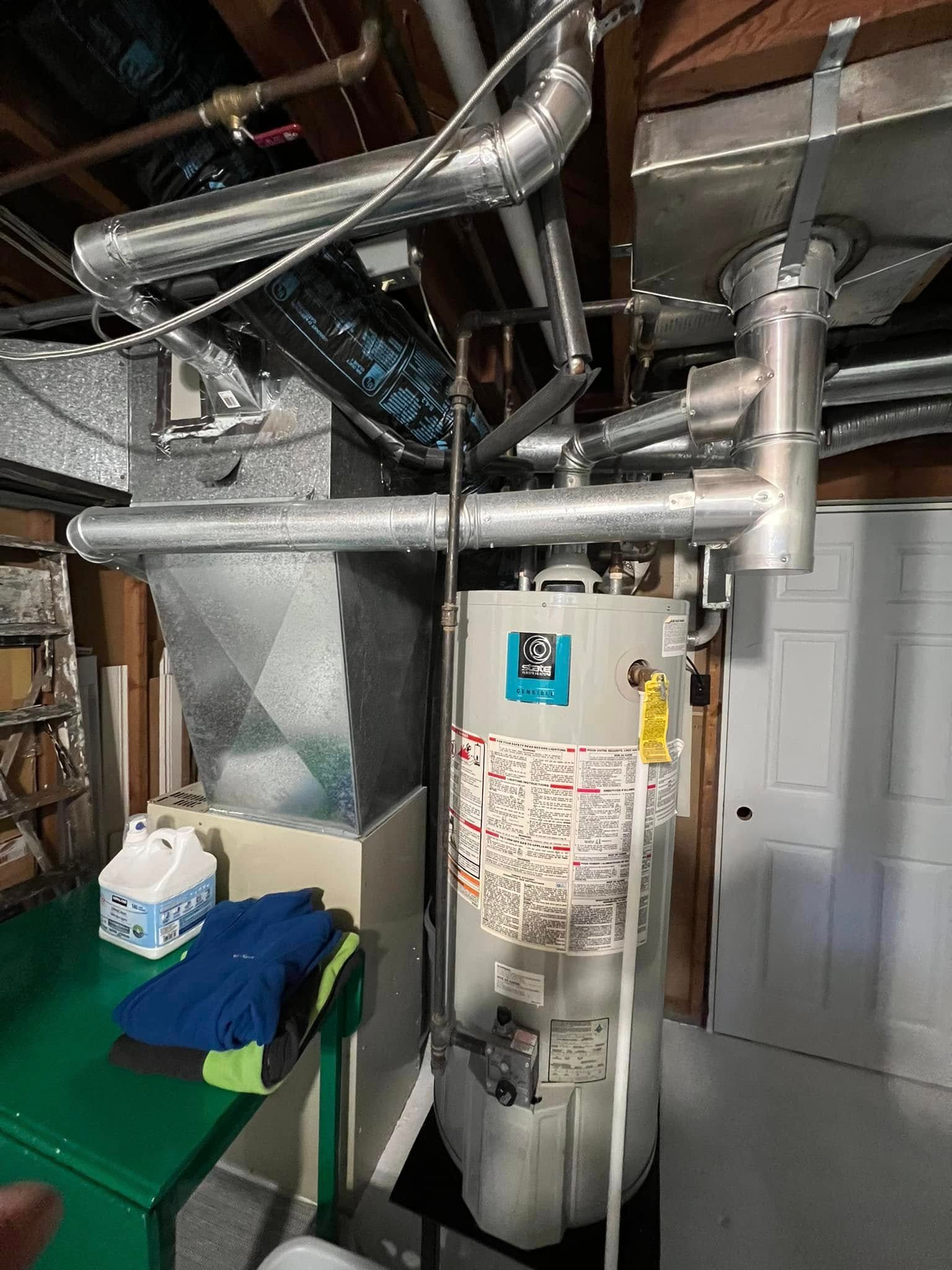 Water heater and furnace with ductwork in a basement room with a green table and folded clothes.