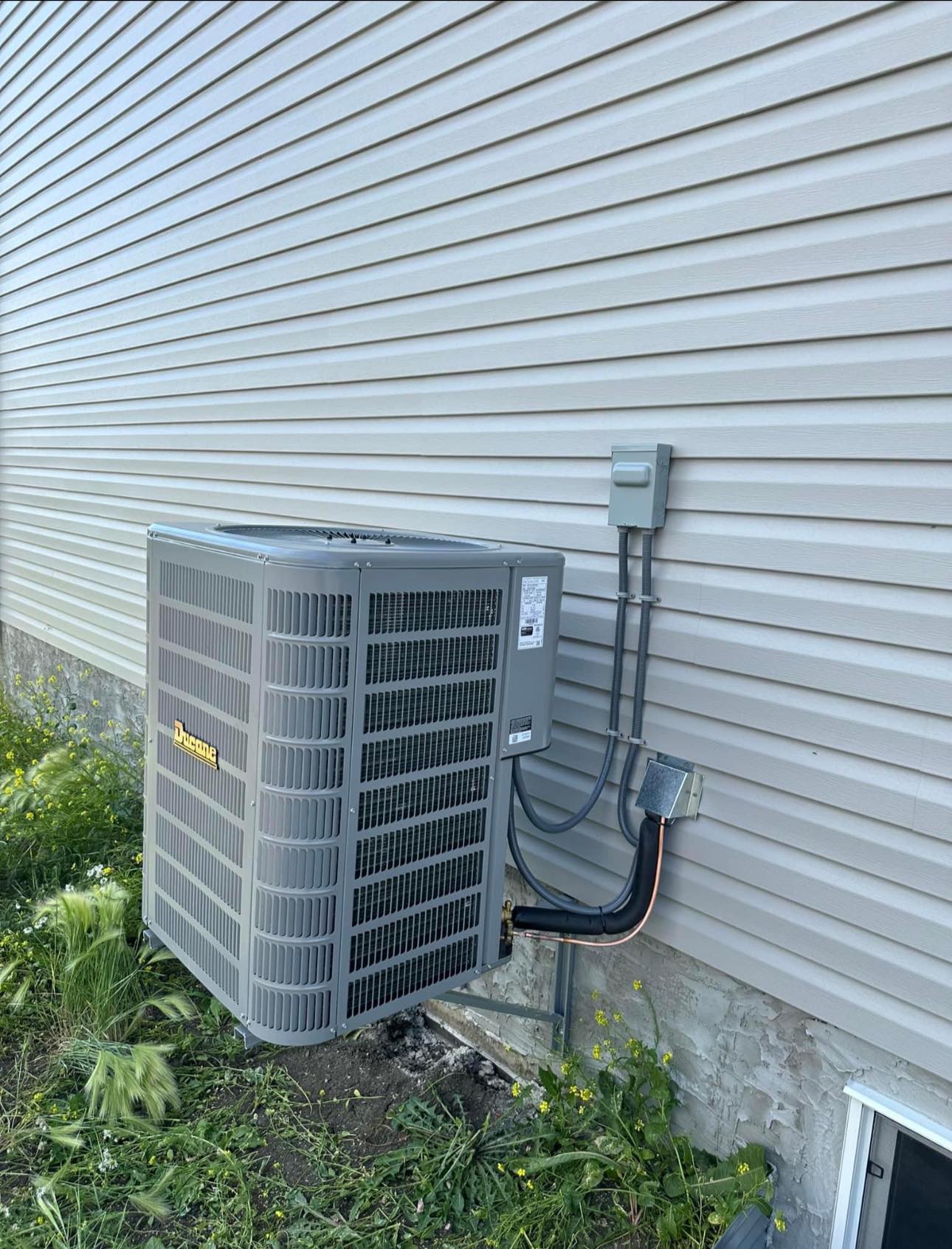 Outdoor gray Ducane air conditioning unit installed on house exterior wall with siding.