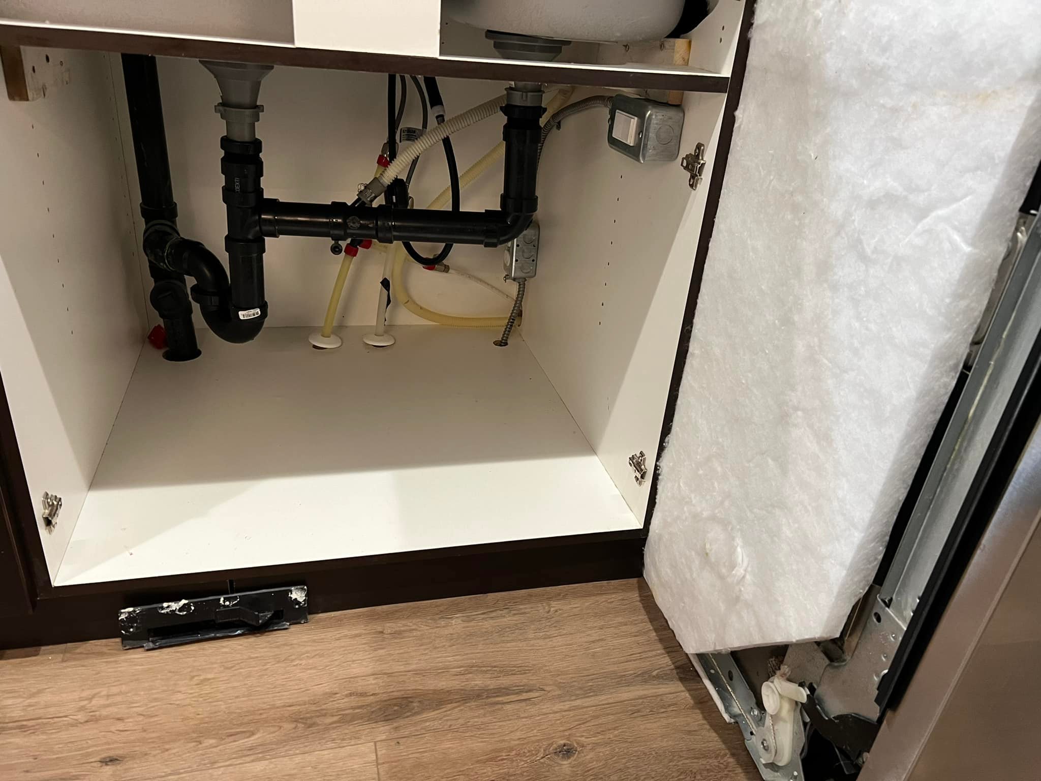Empty kitchen cabinet under sink with exposed black plumbing and white interior.