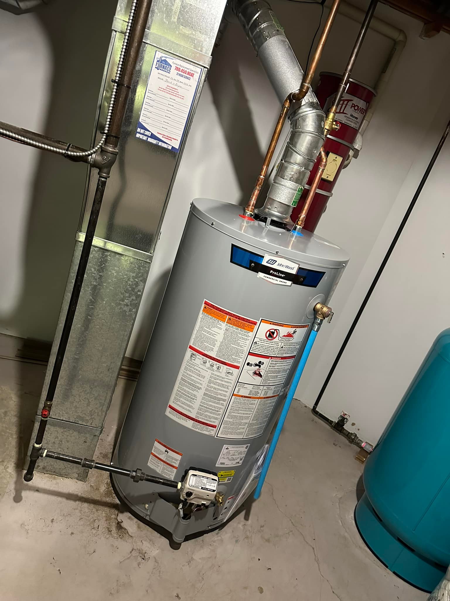 Gray John Wood ProLine water heater with pipes and warning labels installed in a basement.