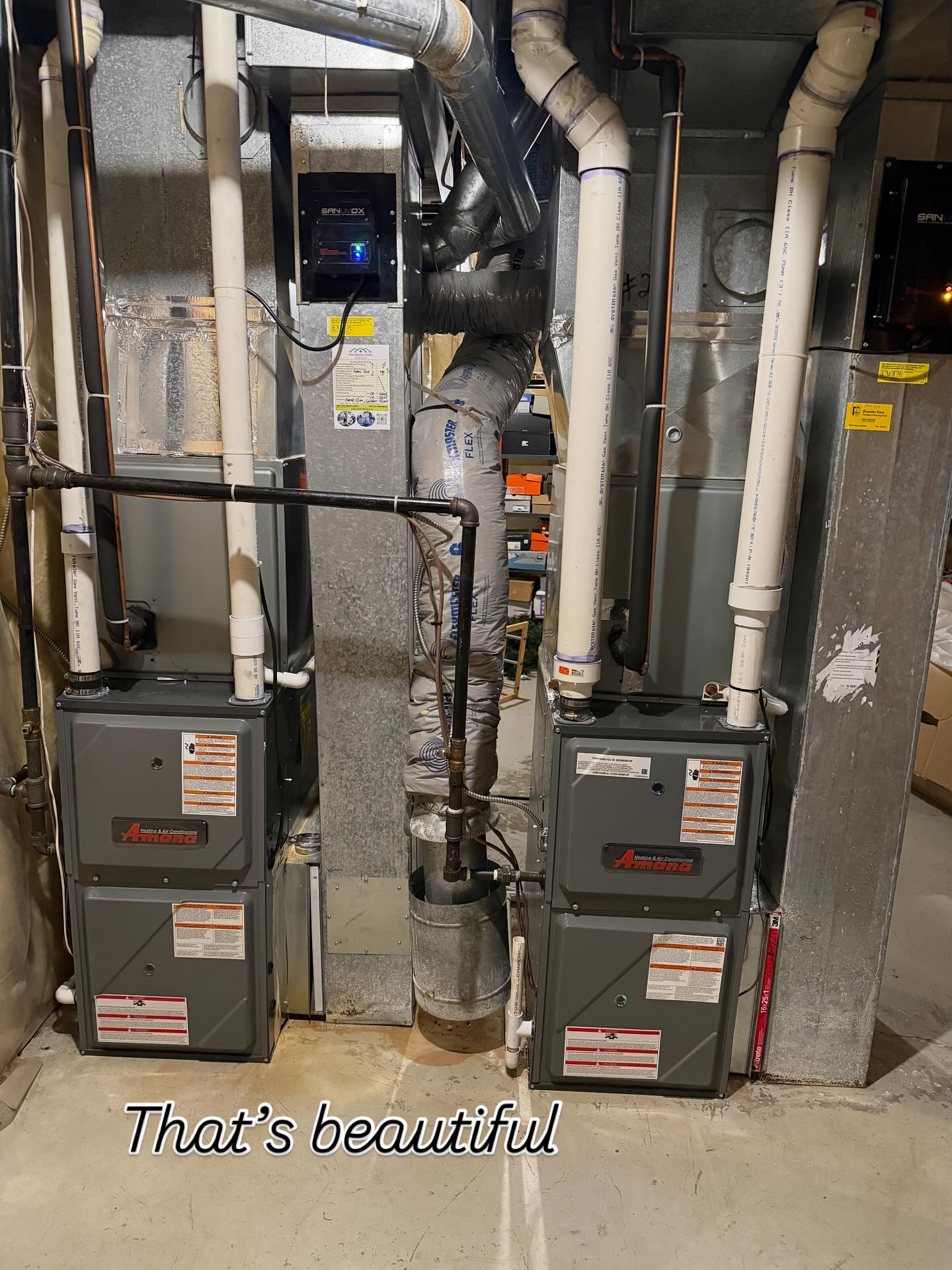Two Amana heating and air conditioning units installed side by side in a basement.