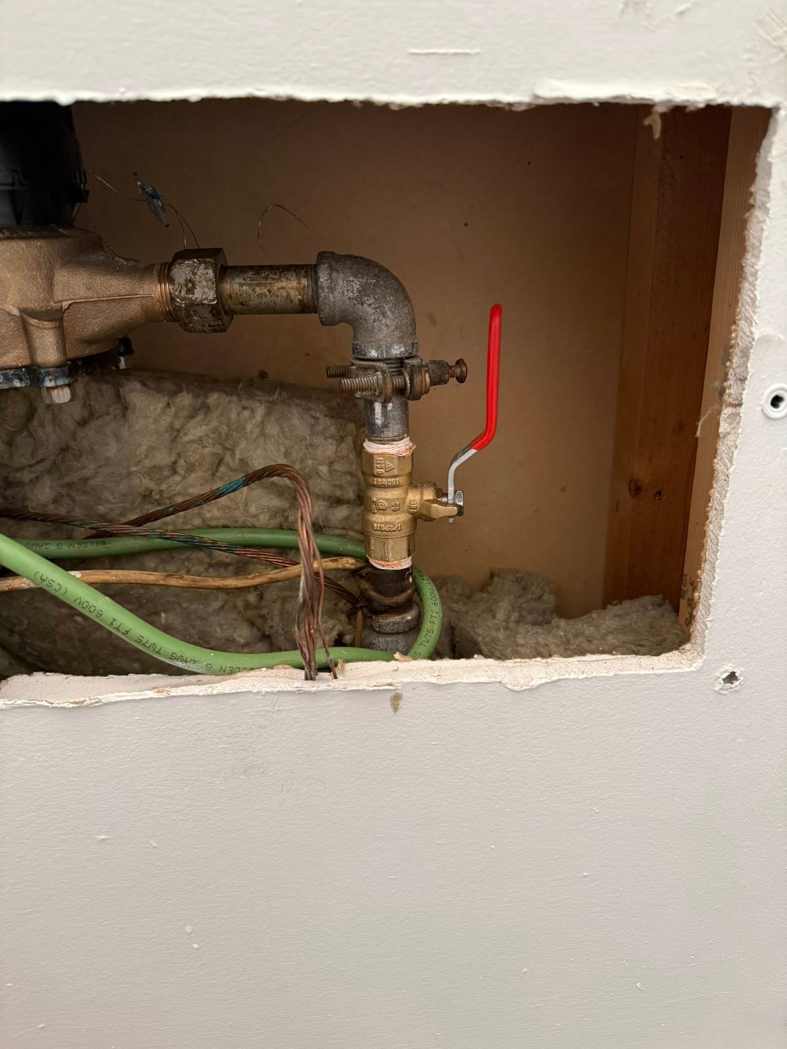 Section of wall opened showing insulated pipes with a valve having a red handle inside the wall cavity.