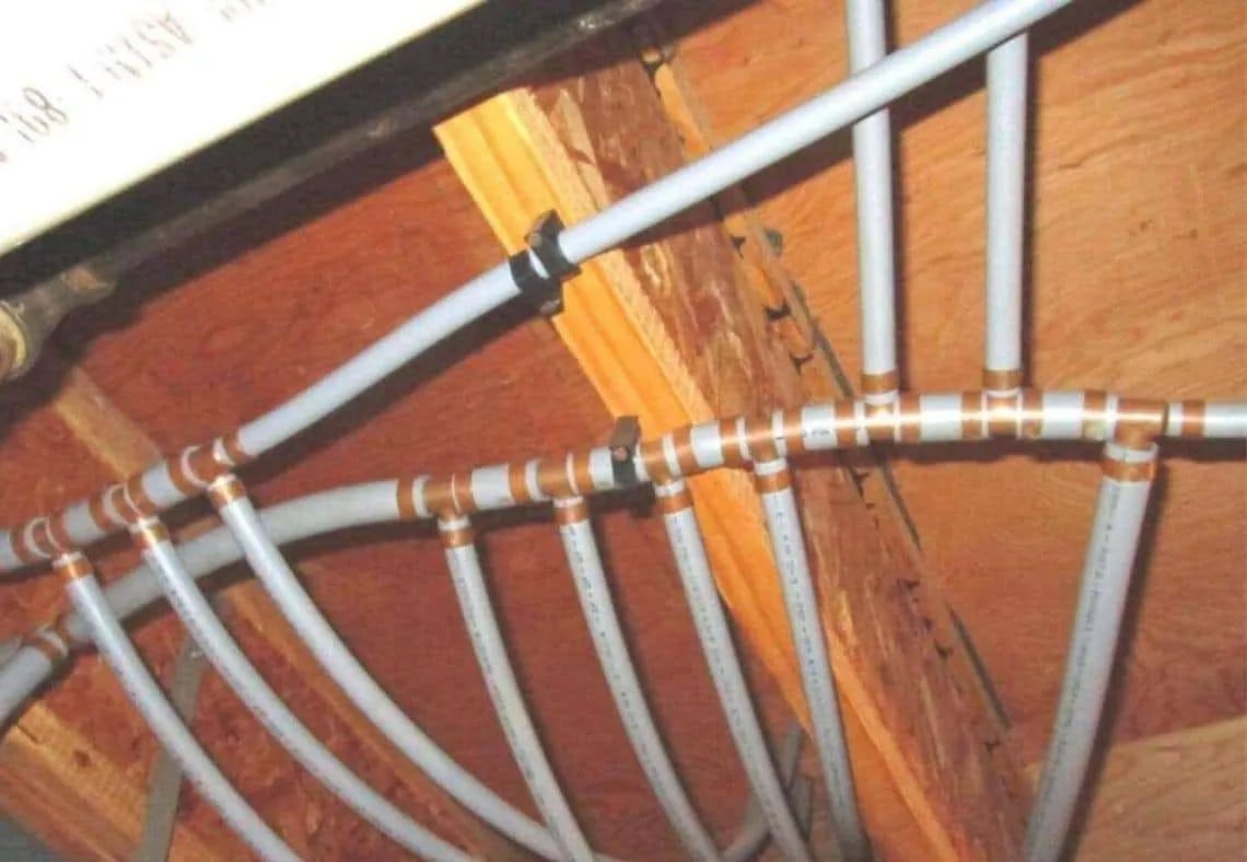 Multiple PEX water pipes connected with copper fittings installed along wooden beams in a ceiling space.