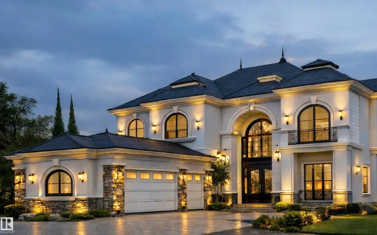 Large two-story luxury house with arched windows, stone accents, and warm exterior lighting at dusk.