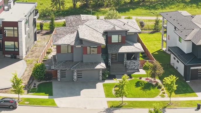 A modern two-story house with gray exterior, stone accents, driveway, and green front lawn.