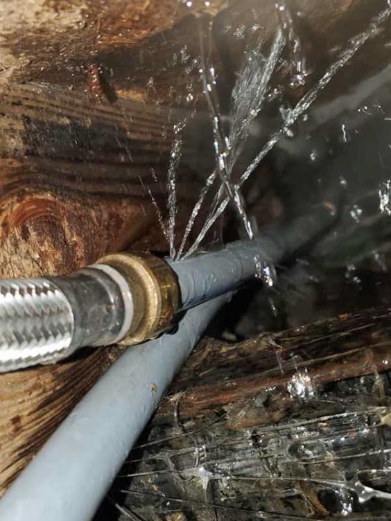 Close-up of a leaking pipe with water spraying out through multiple cracks.
