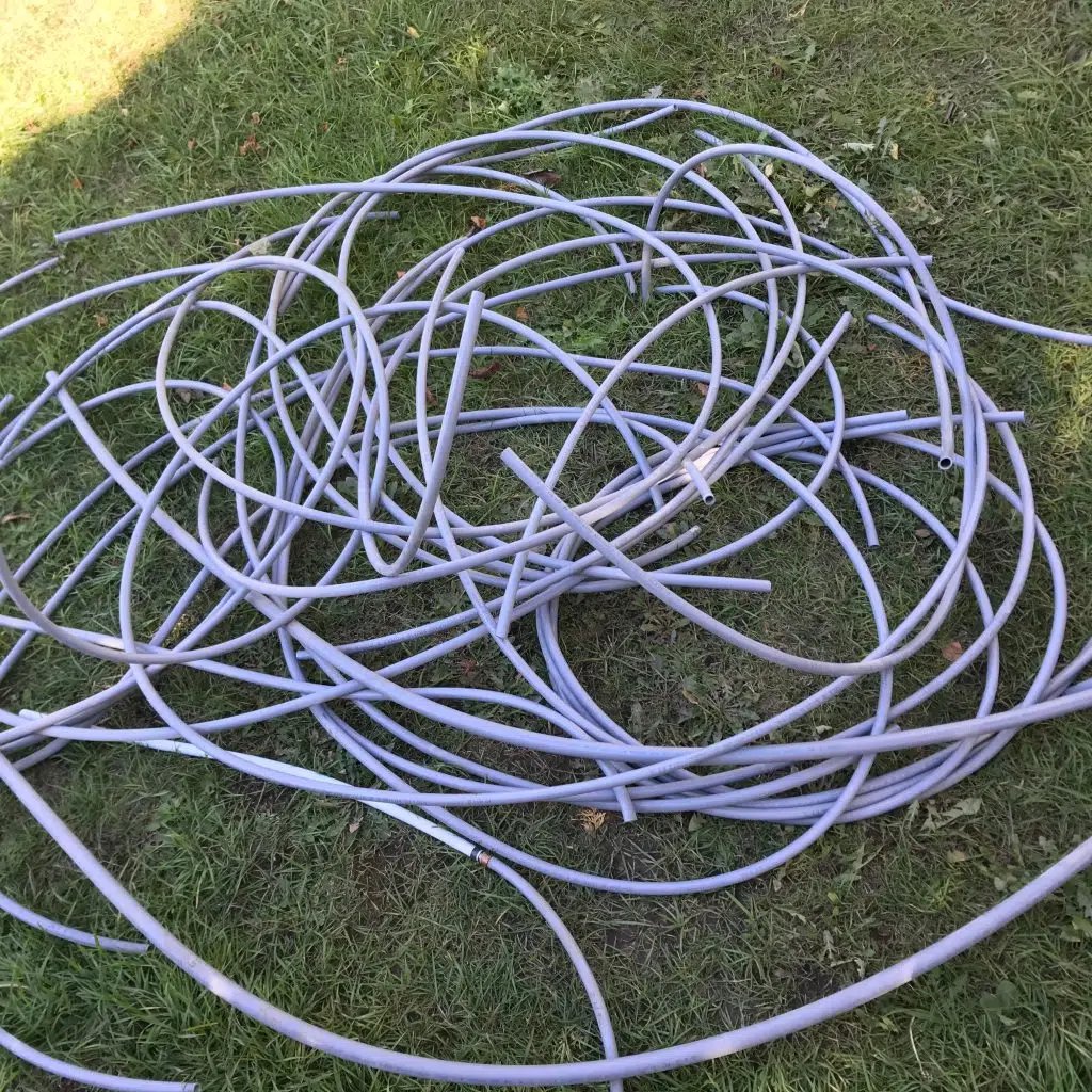 Coiled and tangled gray plastic tubing lying on green grass outdoors.