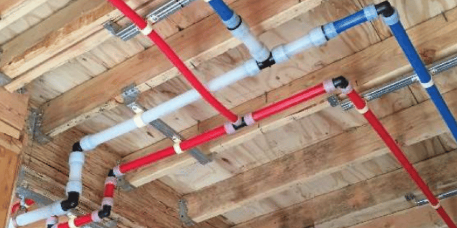 Red, blue, and white plumbing pipes fixed on a wooden ceiling with metal brackets.